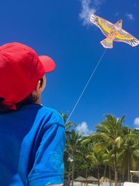 Low angle view of boy flying kite against blue sky