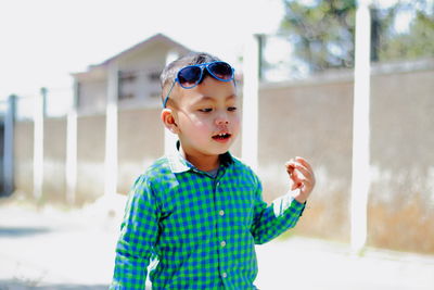 Boy wearing sunglasses standing against built structure