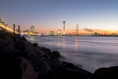 View of illuminated buildings by sea against sky during sunset