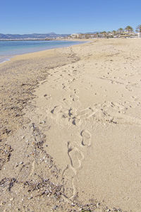 Footprints on sand at beach against clear sky