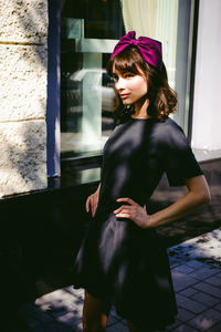 Beautiful young woman in black dress standing by building