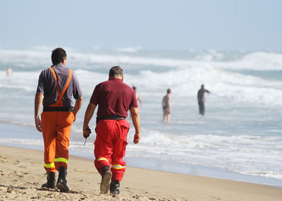 Rear view of men walking at beach