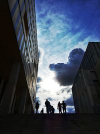 Low angle view of silhouette people walking on modern buildings against sky