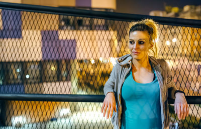 Portrait of woman athlete wearing casual sportswear resting over banister at night in urban setting