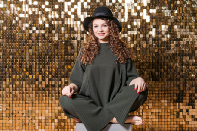 Beautiful young woman in black hat on background shiny golden wall, smiles