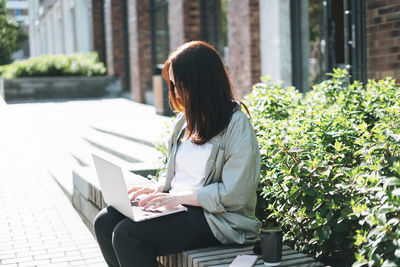 Adult business woman forty years in stylish shirt working on laptop at public place on bench at city 