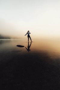 Silhouette of young caucasian woman touching the water with legs in the foggy forest lake at sunrise