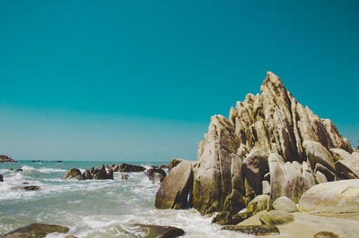 Rocks on beach against clear blue sky
