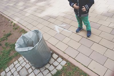 Low section of boy standing on walkway by garbage bin