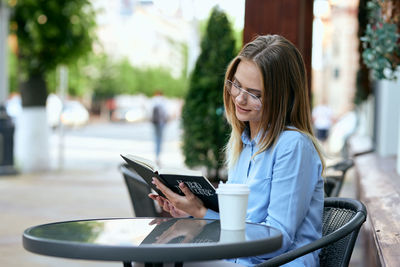 Young woman using mobile phone while sitting on table