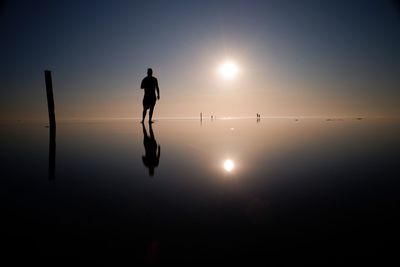Silhouette man standing in water against sky during sunset