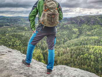 Climber man with backpack and trekking clothes on the top of a hill, agains mountains.