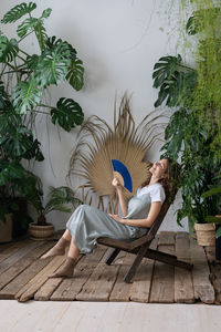 Young relaxed dreamy woman using paper fan while relaxing in beautiful refreshing home garden