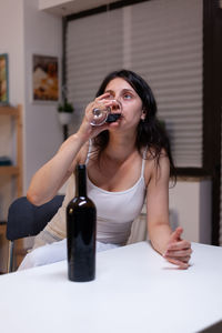 Portrait of young woman drinking glasses on table at home