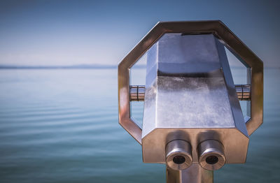 Close-up of coin-operated binoculars by sea against sky