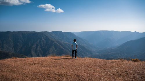 Rear view of man looking at view while standing against mountain range