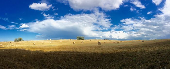 Hay bales on field against cloudy sky