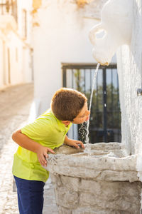 Thirsty kid drinking of an ancient fountain