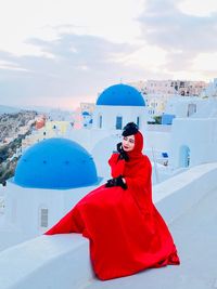 Woman on red dress sitting on the rooftop with the background of  blue sky and ocean