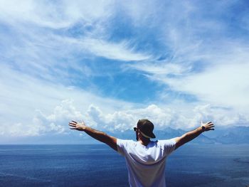 Rear view of man with arms outstretched by sea against sky