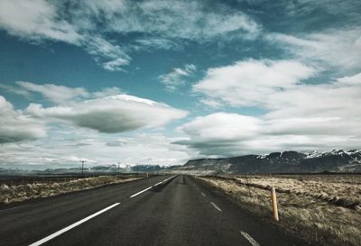 Empty country road against cloudy sky