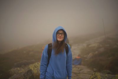 Portrait of smiling young woman standing against sky during winter