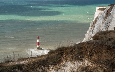 Lighthouse on beach by sea against buildings