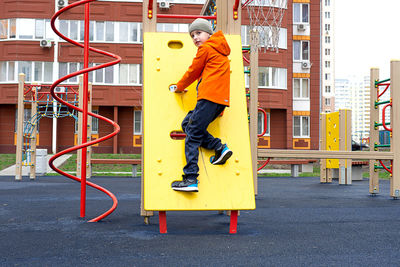 Funny caucasian blond boy in an orange jacket plays on the sports playground