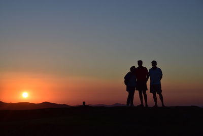Silhouette of people on mountain at sunset