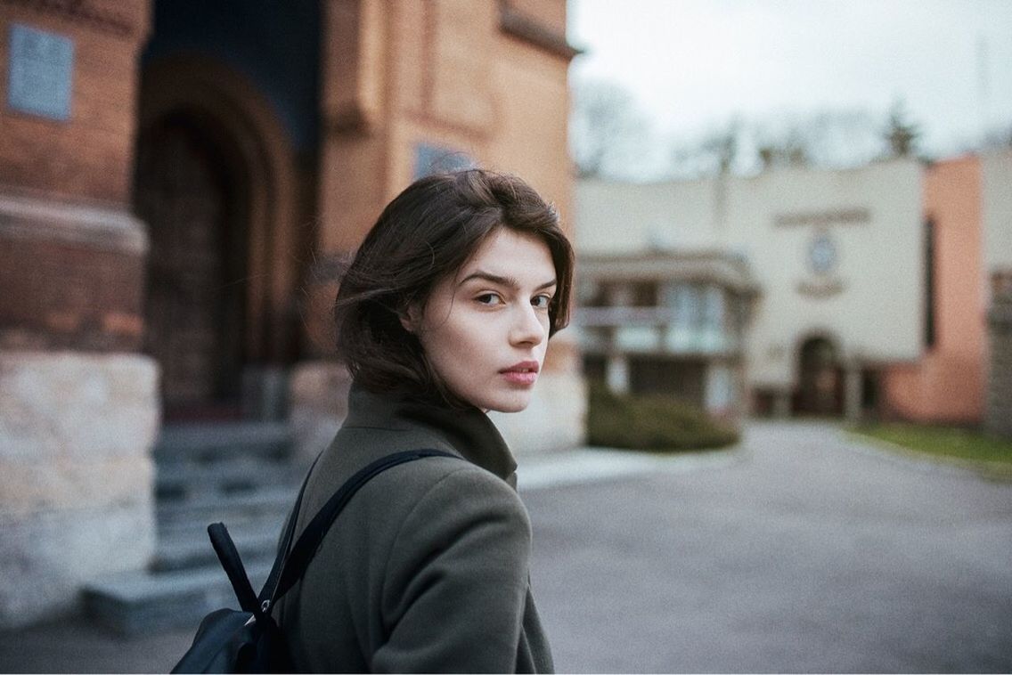 architecture, built structure, one person, building exterior, focus on foreground, city, portrait, young adult, standing, women, adult, young women, building, looking, real people, day, street, side view, looking at camera, beautiful woman, contemplation, outdoors, hairstyle, warm clothing