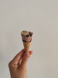 Cropped image of person holding ice cream cone against wall