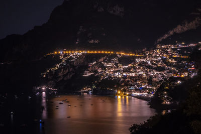 Illuminated city by river against sky at night