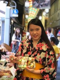 Portrait of young woman wearing kimono holding packet at market