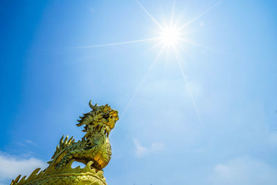 Low angle view of dragon statue against blue sky on sunny day