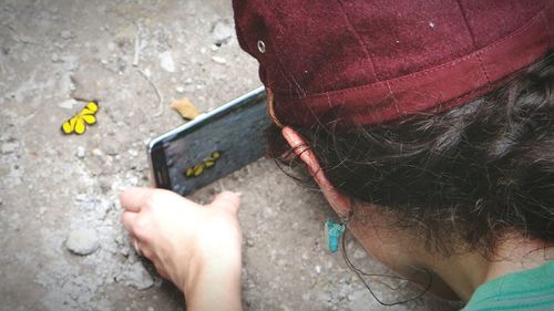 Rear view of woman photographing butterfly with smart phone on ground