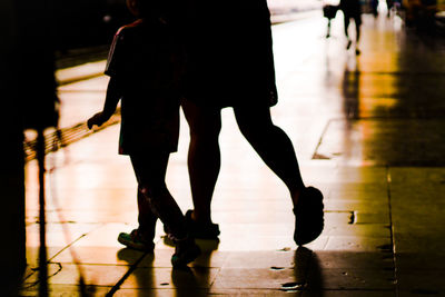 Low section of silhouette woman with son walking on railroad station platform