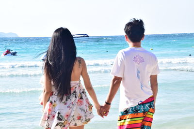 Couple holding hands while standing against sea
