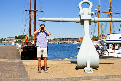 Young man shielding eyes while standing at harbor