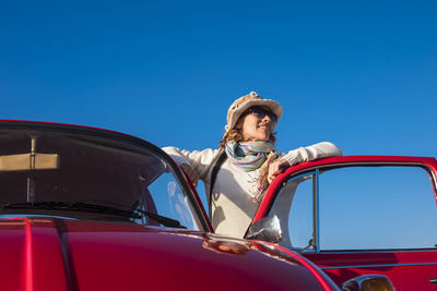 Low angle view of woman standing by car door against clear blue sky