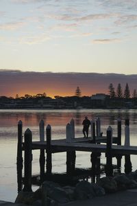 Silhouette man on pier by sea against sky during sunset