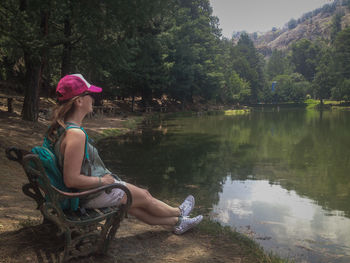 Side view of woman sitting by lake against trees