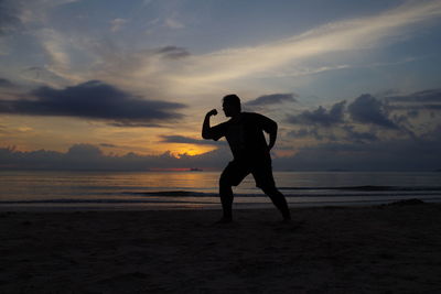 Full length of man exercising on beach against sky during sunset