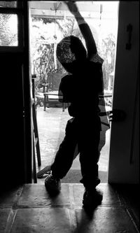 Rear view of boy standing by window at home