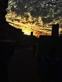 Silhouette people on street against sky at sunset