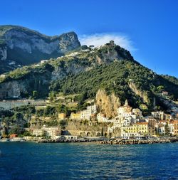 Aerial view of townscape by sea against blue sky