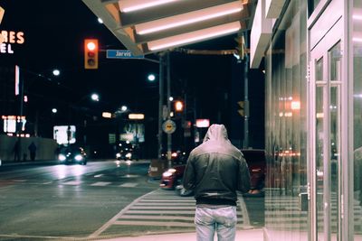 Rear view of man walking in illuminated city at night