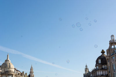 Low angle view of bubbles and buildings against clear blue sky