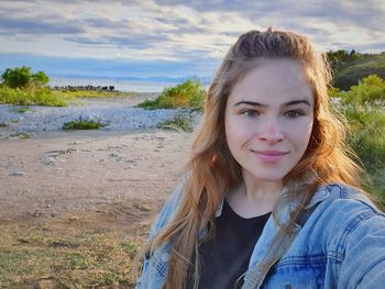 Portrait of smiling young woman lying on land against sky