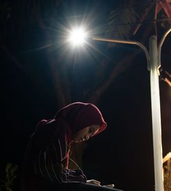 Side view of woman against illuminated light