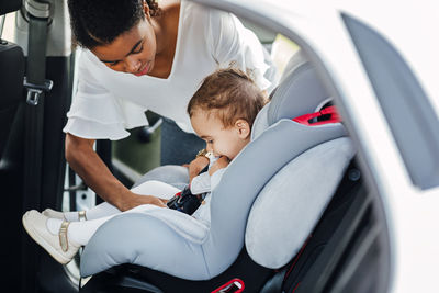 Baby girl sitting in car while mother standing by door